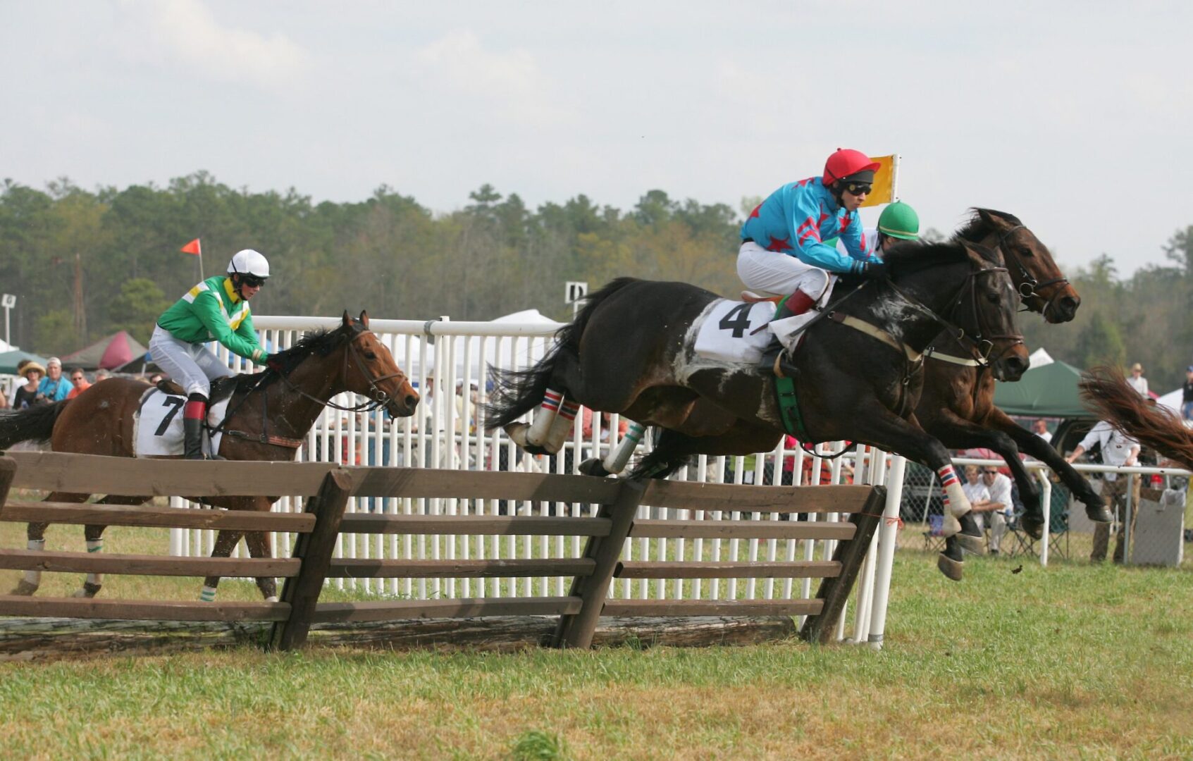 A horse race with two riders jumping over the fence.